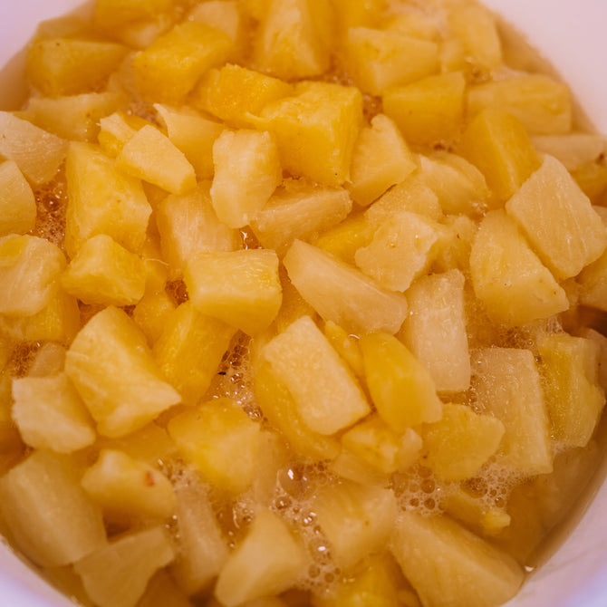 Chopped pineapple pieces in a white bowl or container, photographed from above.
